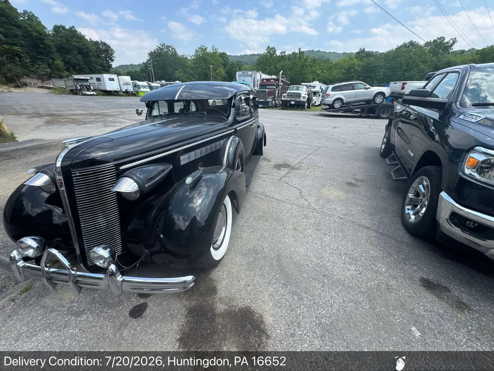 The same black 1930s Buick sedan at delivery in a Huntingdon, Pennsylvania carrier yard, alongside a dually pickup and other transport equipment