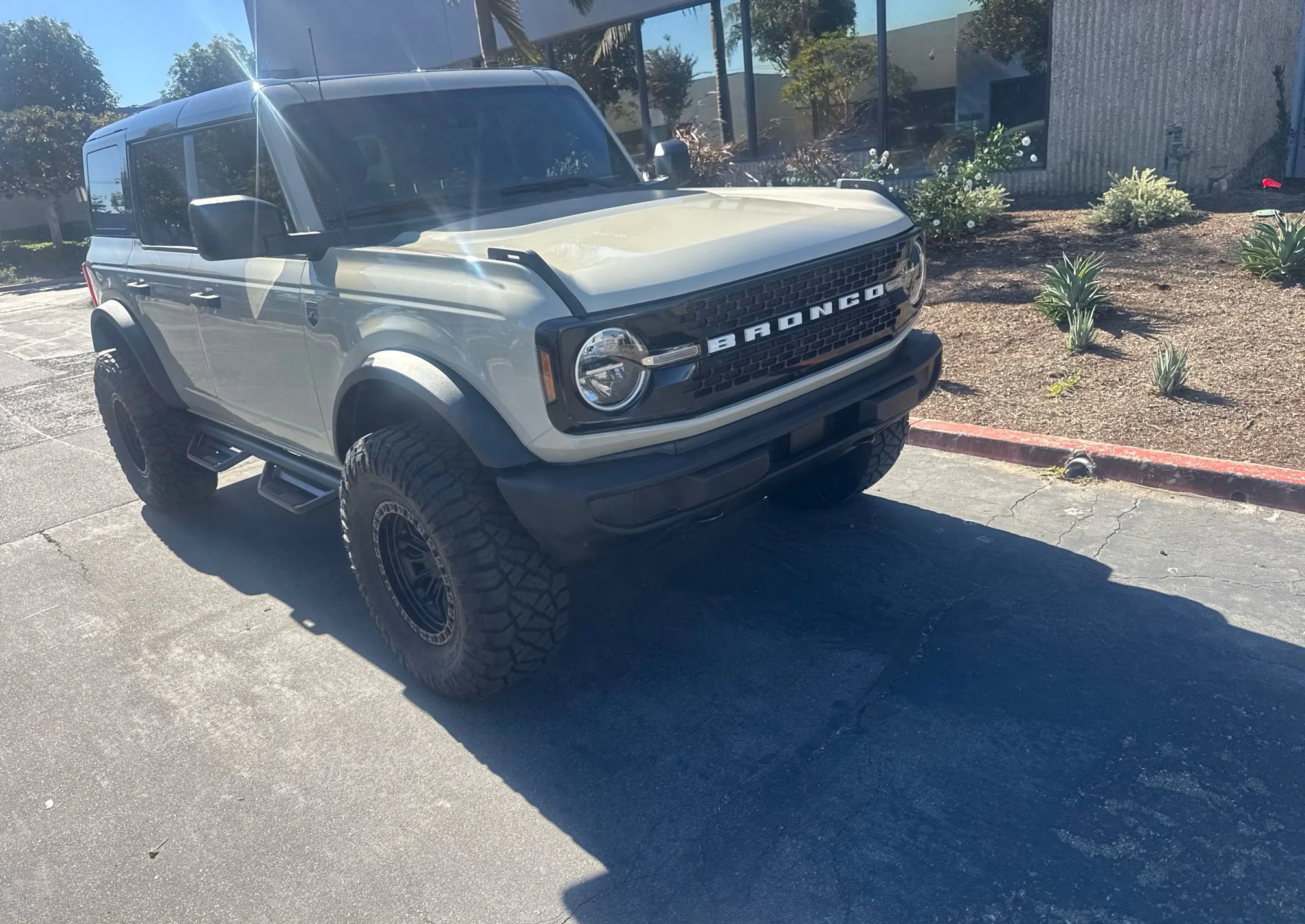 Front three-quarter view of a cream custom Ford Bronco with large off-road tires at pickup in Irvine, California