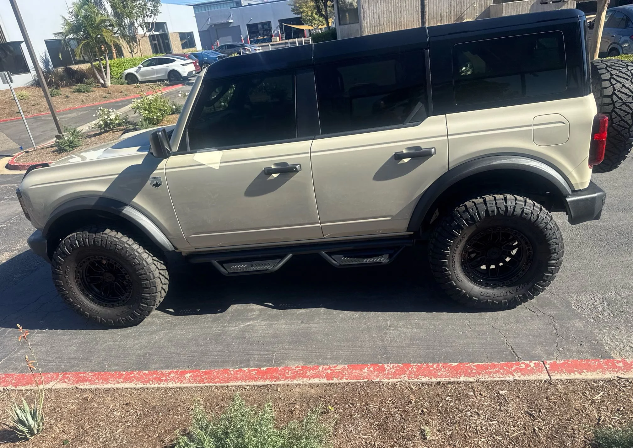 Side view of a custom cream Ford Bronco showing large off-road tires, black wheels and side steps