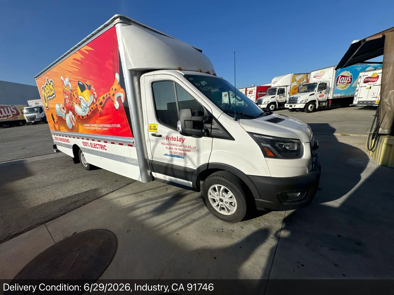 Ford E-Transit electric box truck delivered at a City of Industry, California distribution yard with fleet trucks in the background