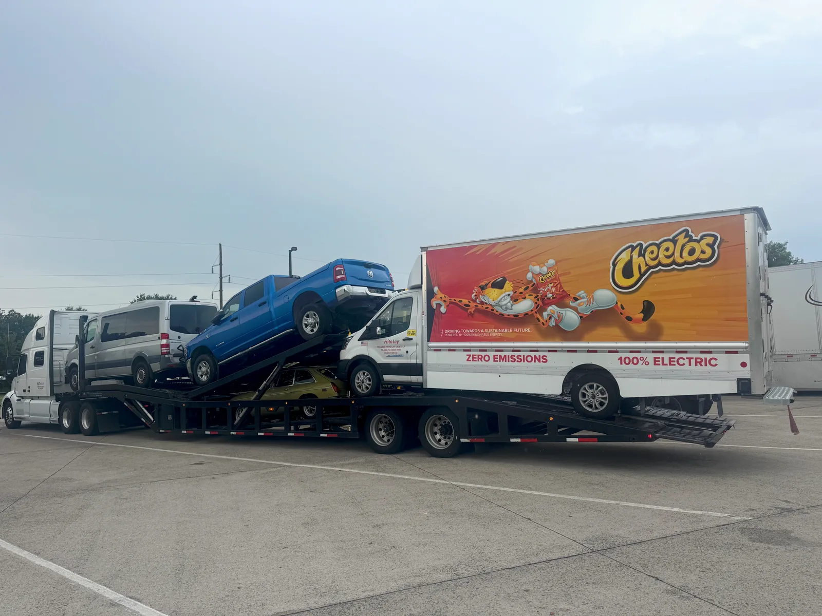 Ford E-Transit electric box truck loaded on the rear slot of an open car hauler with a van and pickup truck