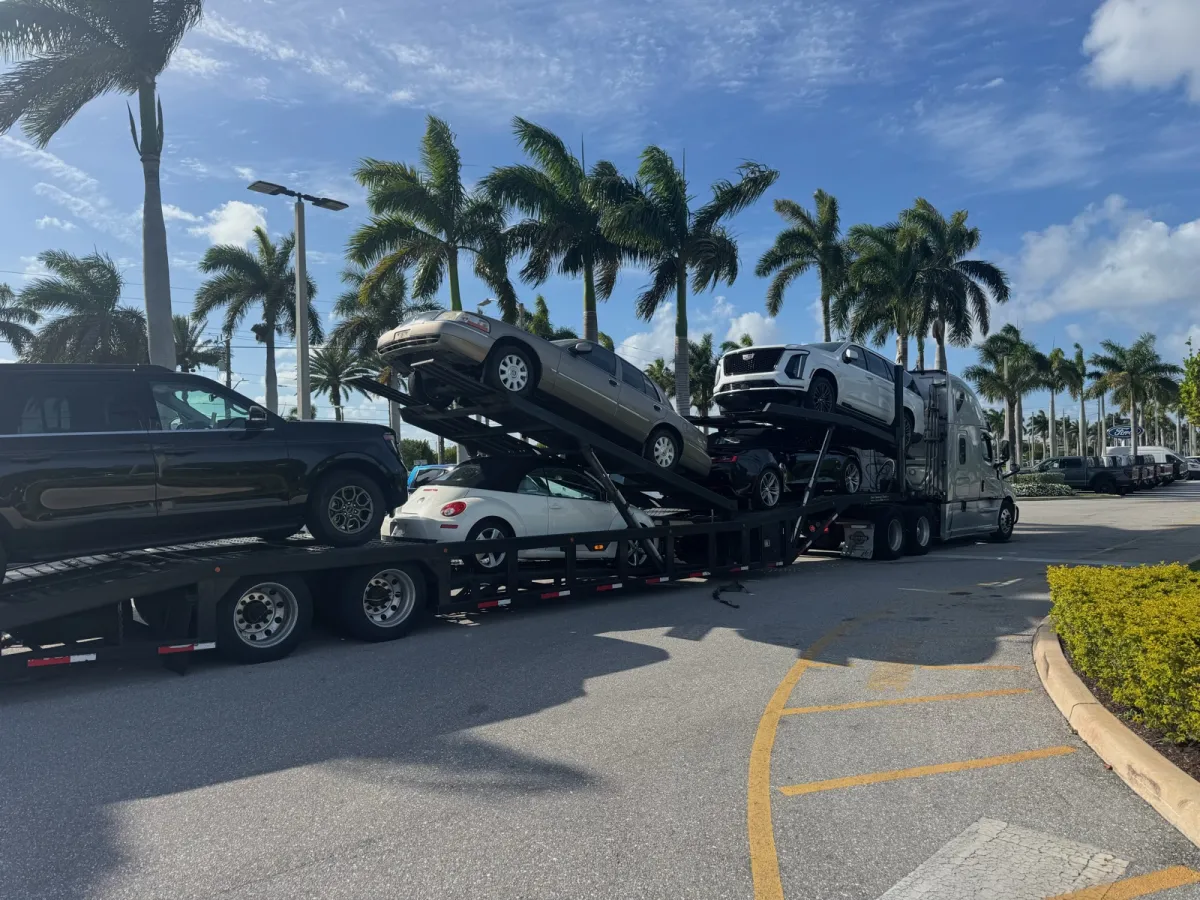 Caravan Transport multi-vehicle carrier delivering cars in South Florida with palm trees in the background