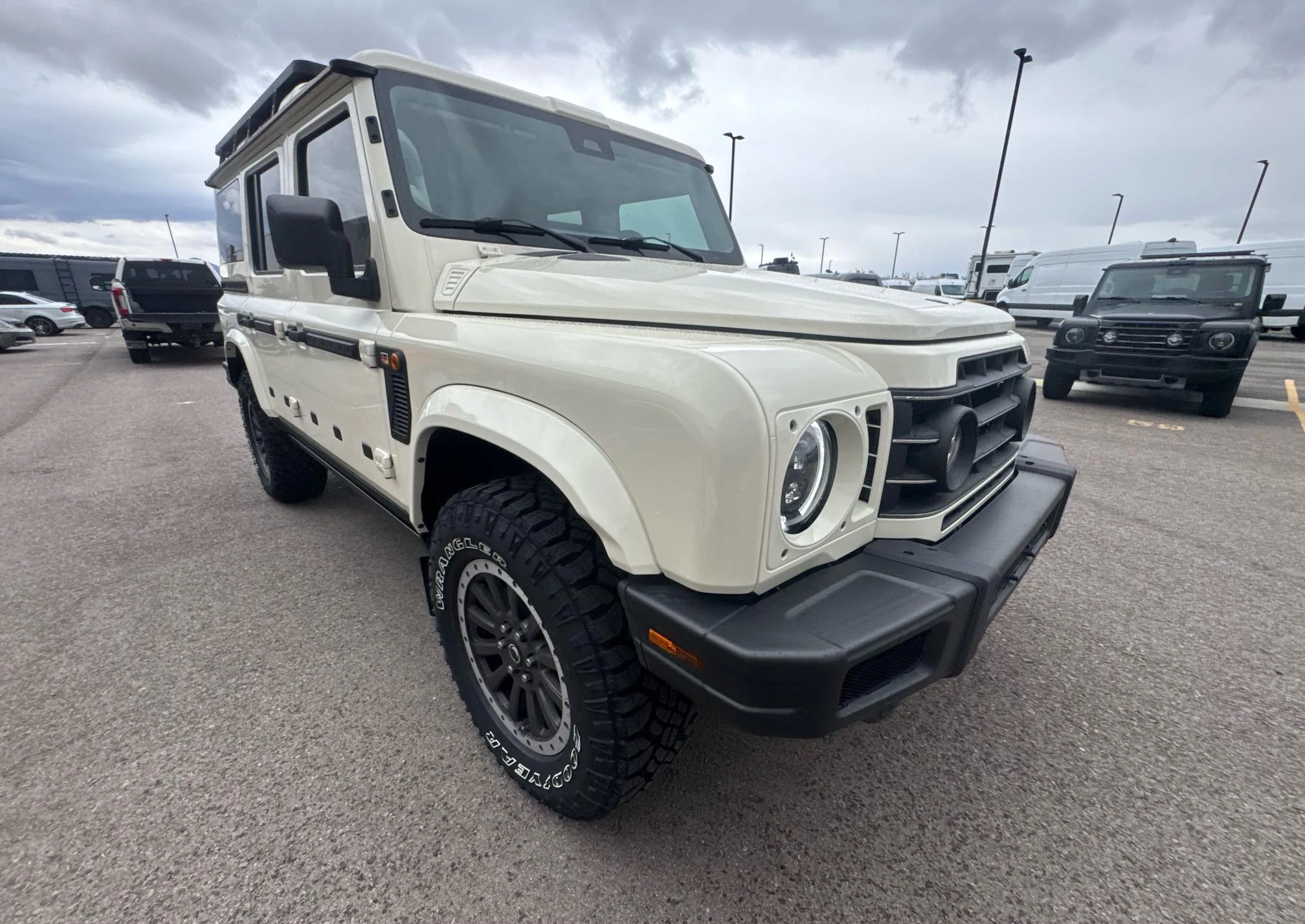 Cream INEOS Grenadier with roof-mounted equipment at a dealership