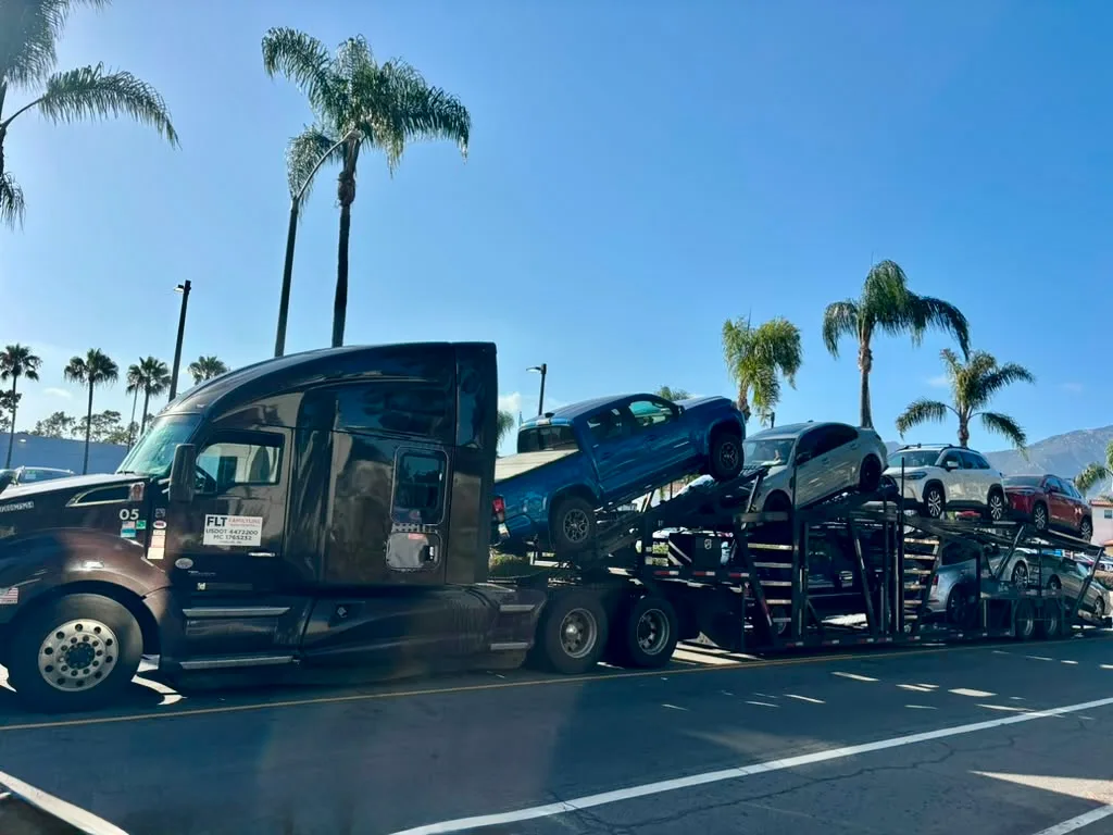 Open car hauler loaded with pickup trucks and SUVs on a palm-lined California street