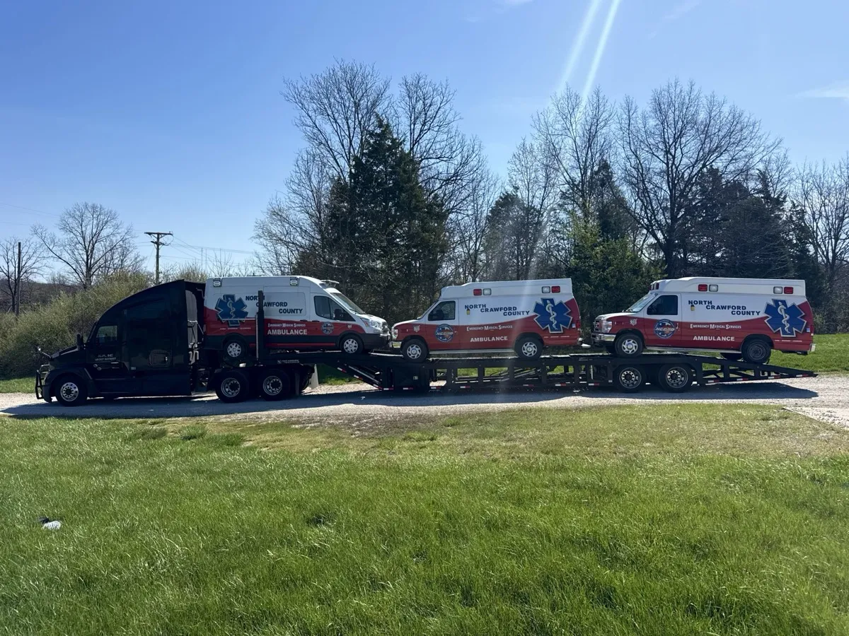 Three ambulance vans loaded on a car carrier for cross-country transport